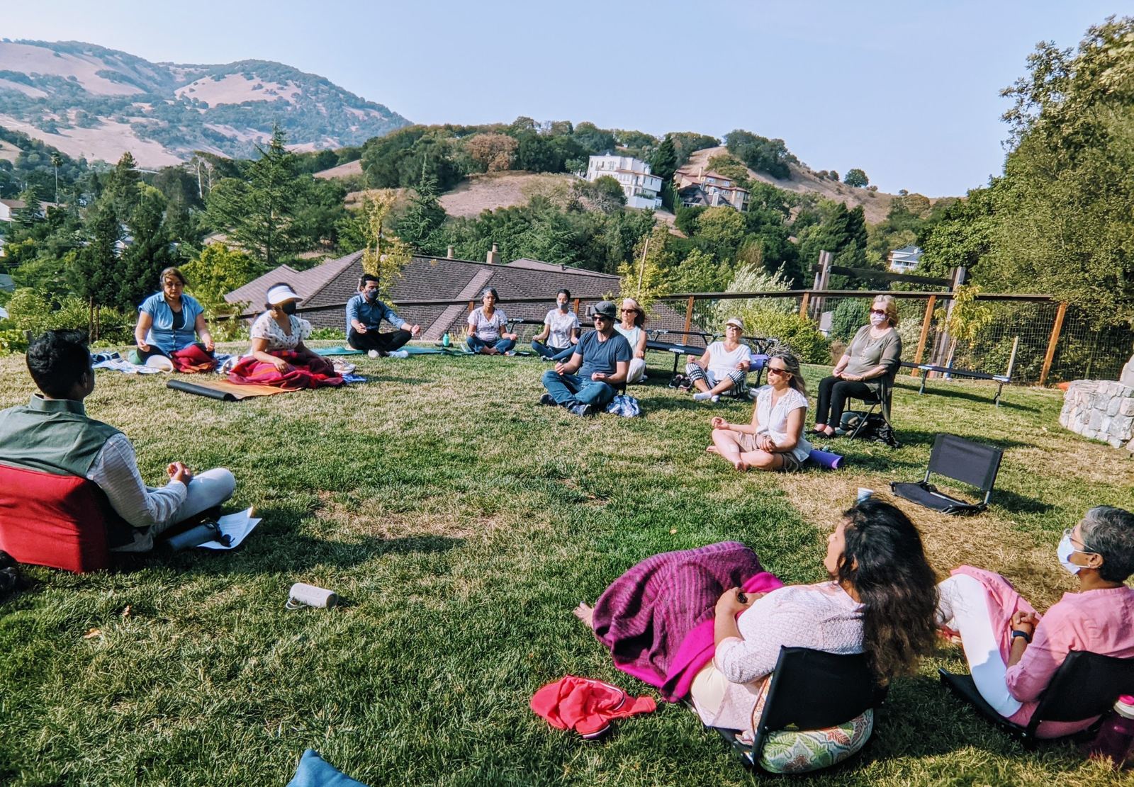 A circle of people meditating on a hillside lawn with Jay