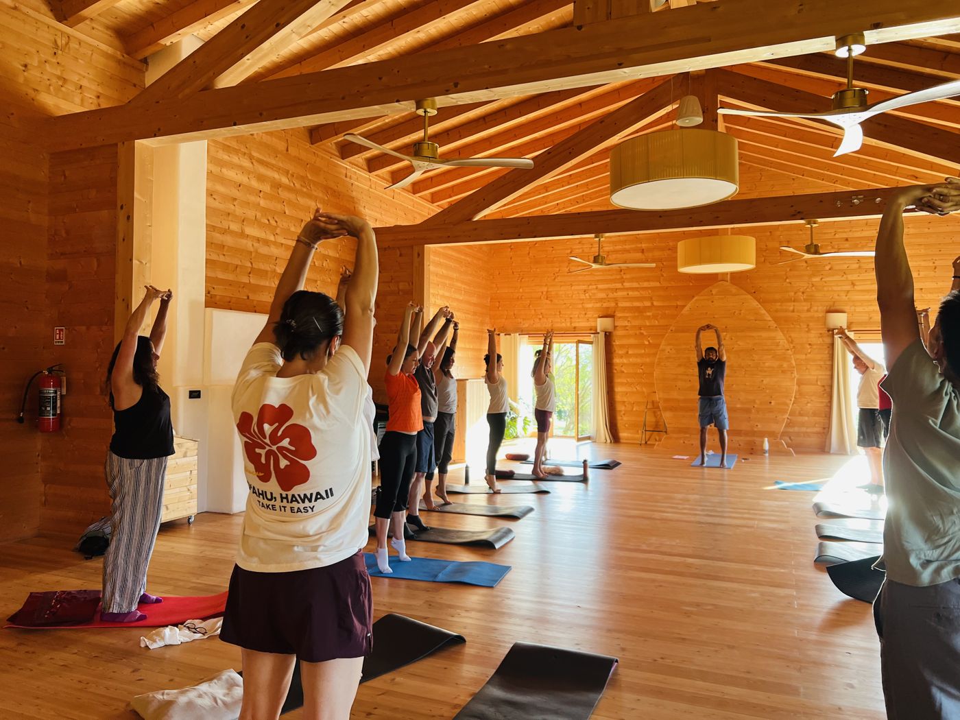 Jay leading a morning yoga stretch in a sunlit wooden hall in Italy
